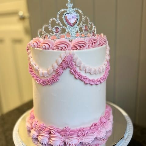 A white cake with pink frosting and a tiara on top.