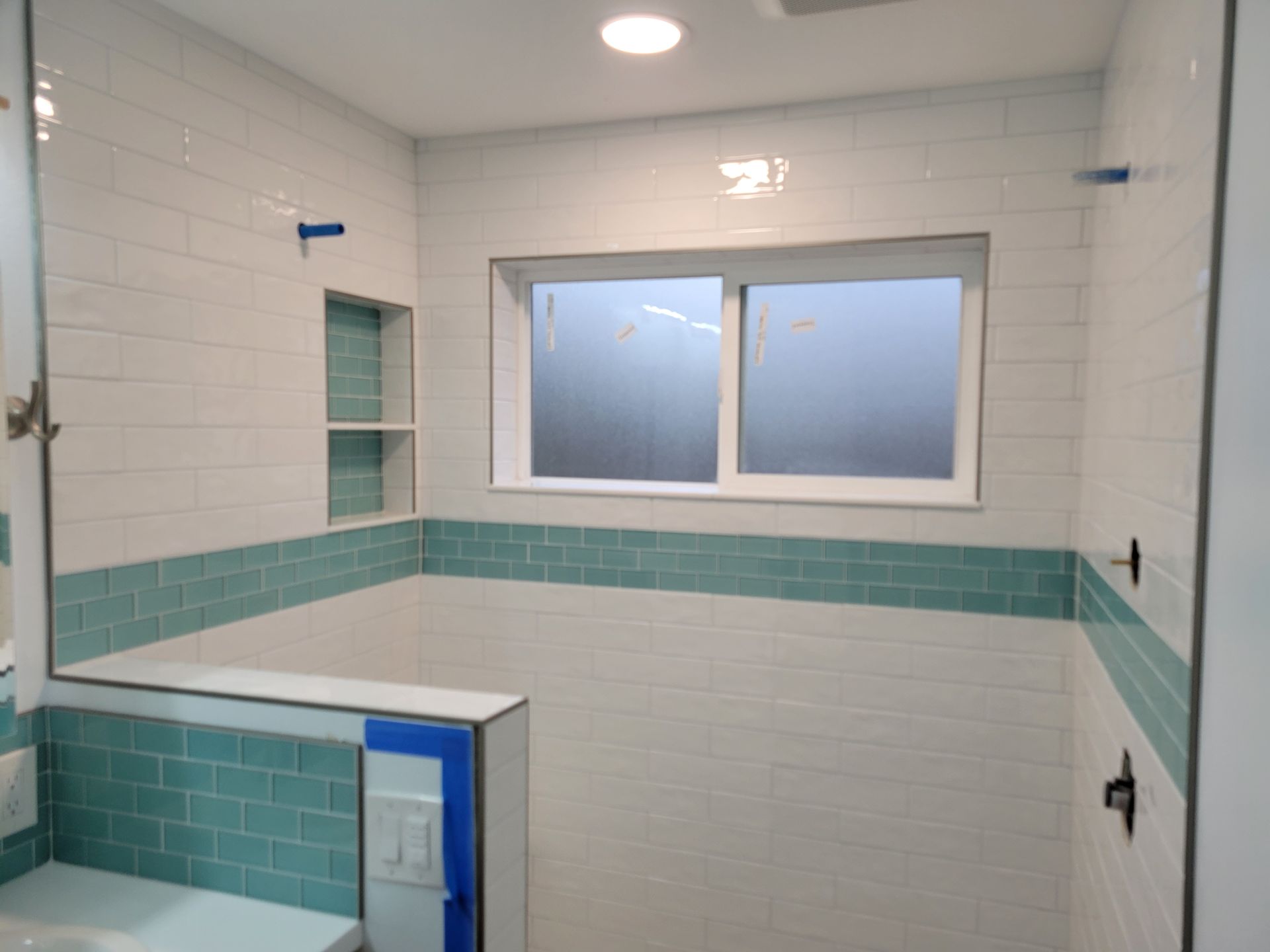 A bathroom with white tiles and blue tiles and a window