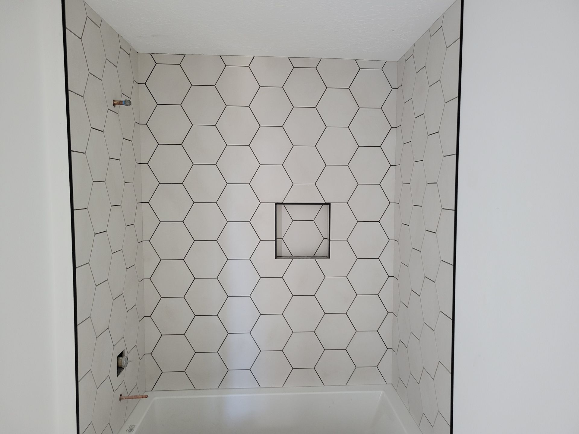 A shower stall with a hexagonal tile pattern on the wall.