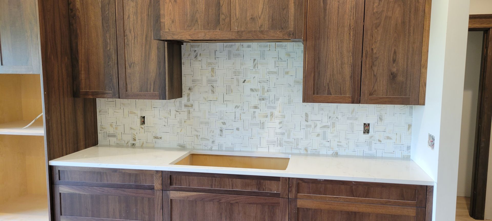 A kitchen with wooden cabinets , white counter tops , and a sink.