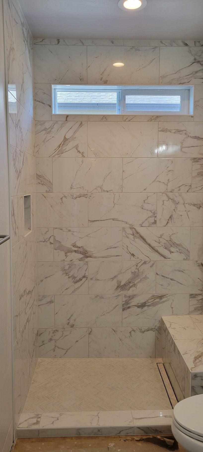 A bathroom with a walk in shower , toilet and window.