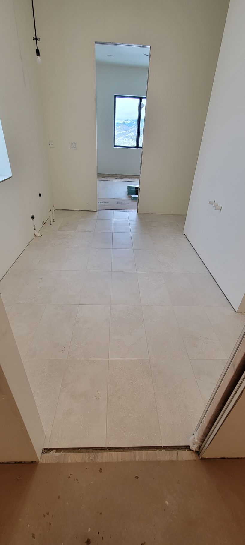 A hallway with tile floors and a window in a house under construction.