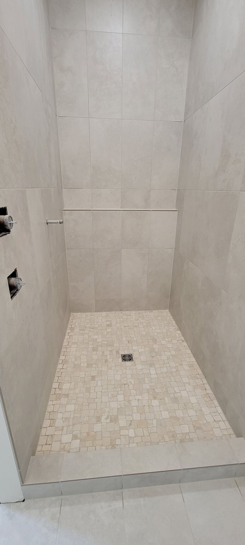A shower stall with a tiled floor and a glass door in a bathroom.
