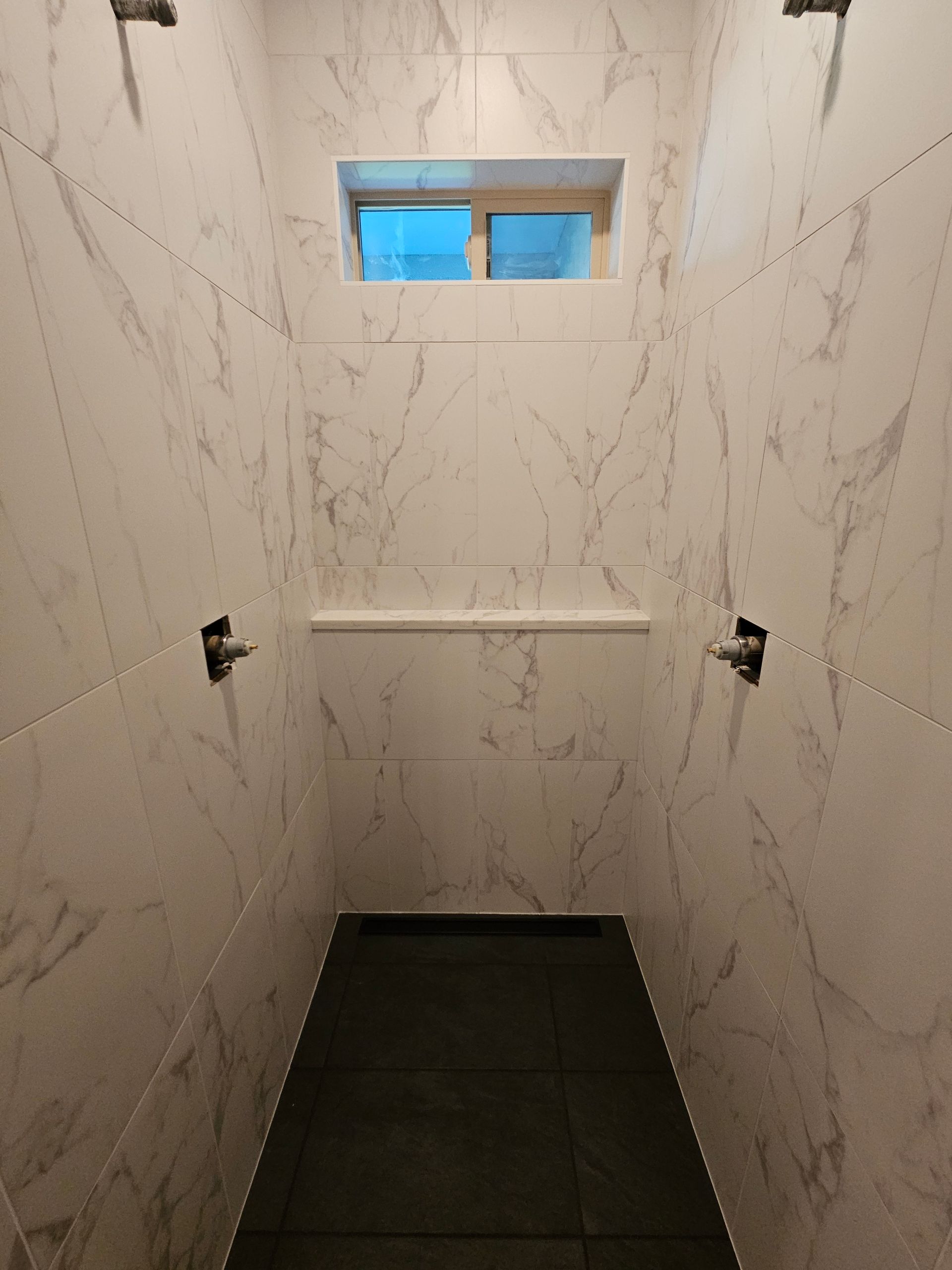 A bathroom with marble walls and a window in the shower.