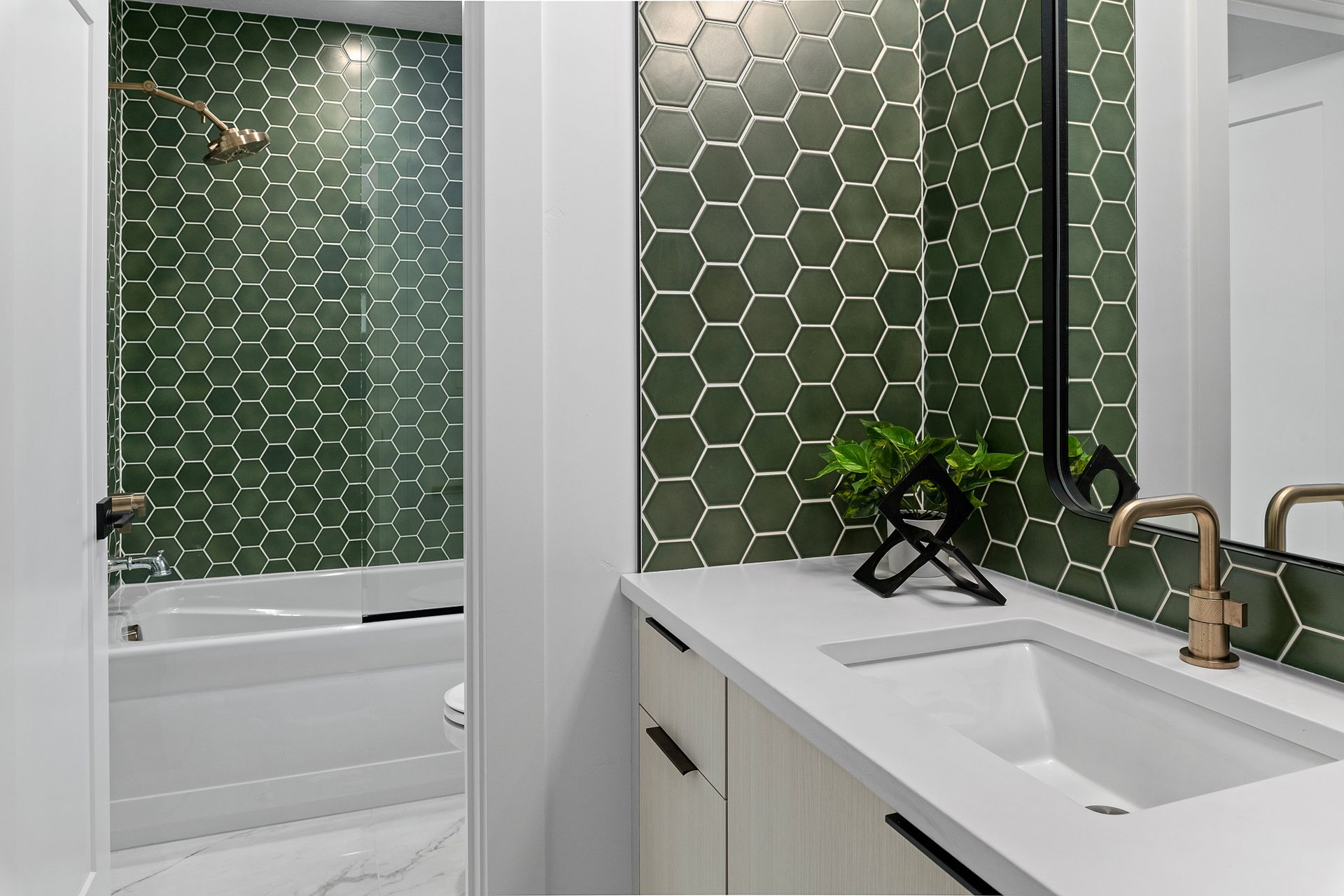 A bathroom with green tiles , a sink , a tub and a mirror.