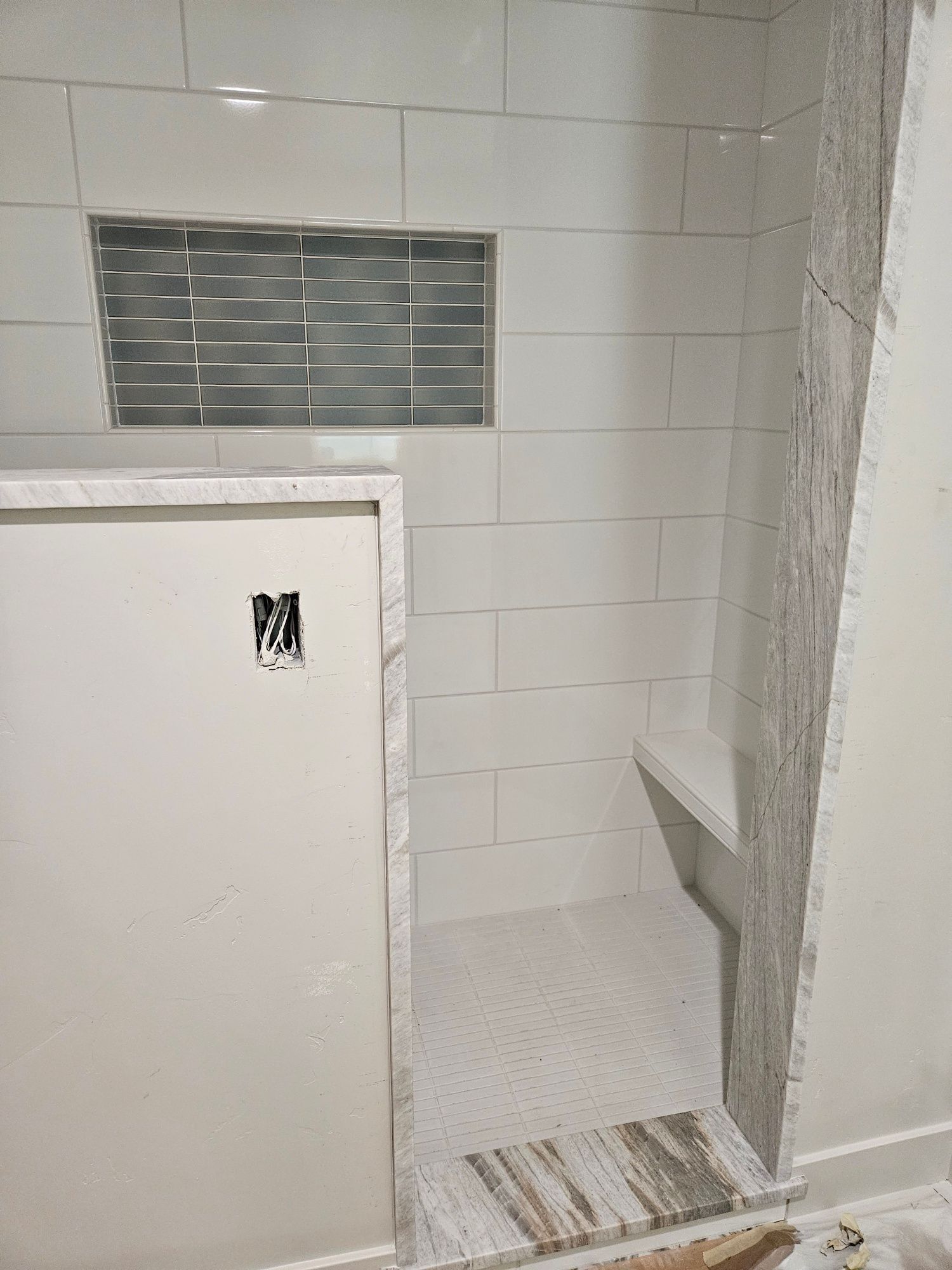 A bathroom with white tiles and a walk in shower with a bench.