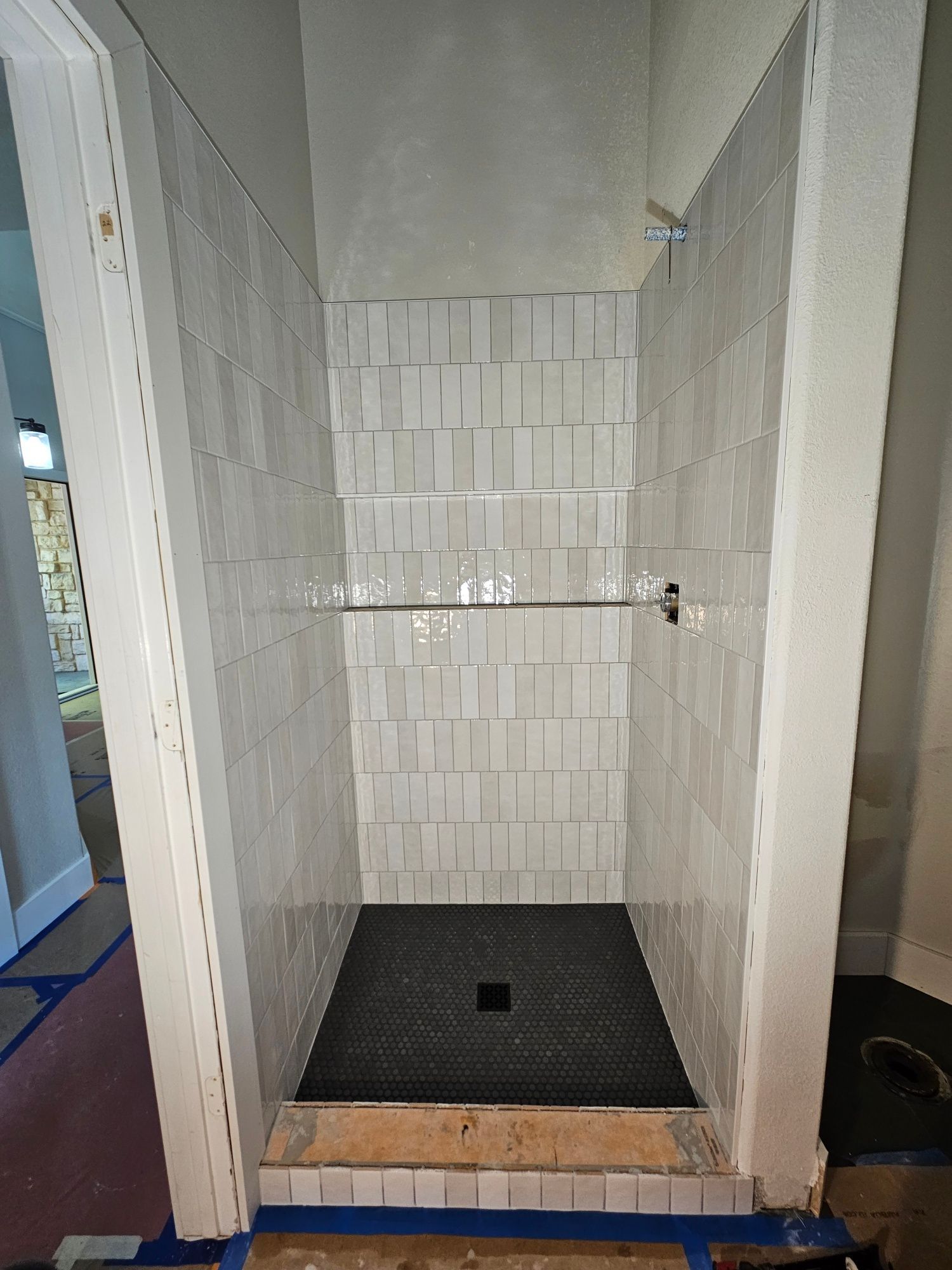 A shower stall with white tiles and a black floor is being built in a bathroom.