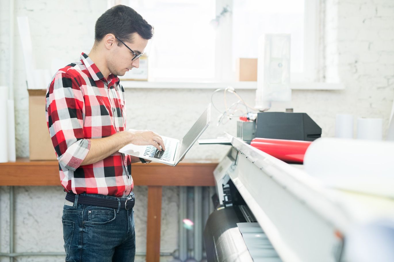 a man using a computer next to a large printer
