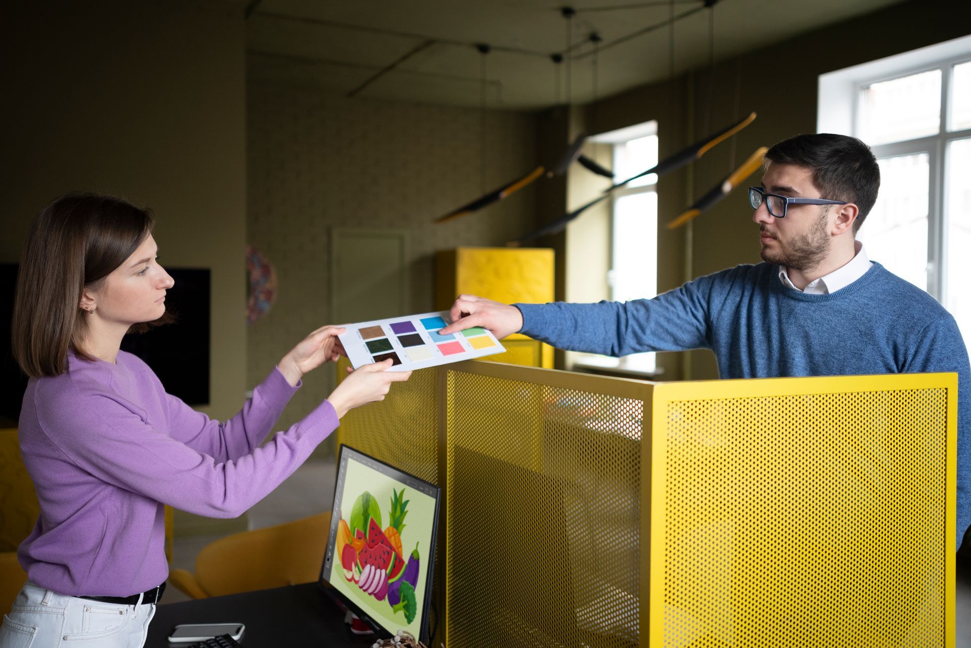 A man and a woman are looking at a color palette in an office.