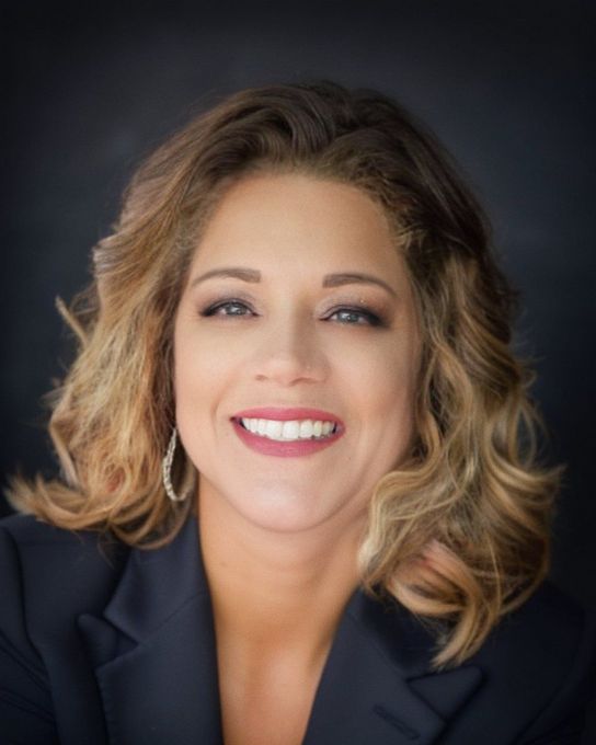 Headshot of Angel Price, Dickinson and Texas City realtor, positioned against a professional backdrop. Angel wears a confident smile, exuding approachability and professionalism. The backdrop suggests a modern office environment, reflecting her dedication to the real estate industry. Her attire is smart and professional, evoking trustworthiness and reliability. The image captures Angel as a knowledgeable and personable real estate agent ready to assist clients in Galveston County.