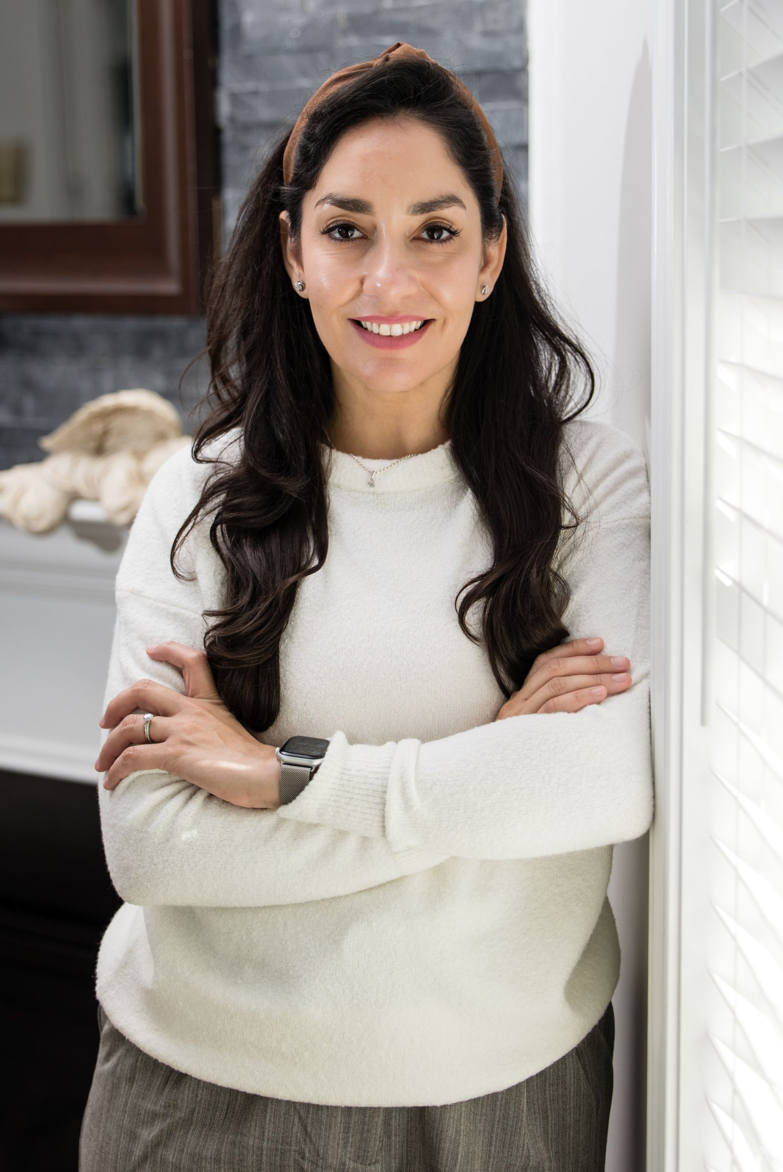 Rose, the Realtor leaning on a wall next to white blinds with her arms folded. 