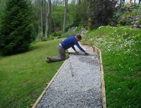 Man working on installing a gravel pathway through a garden