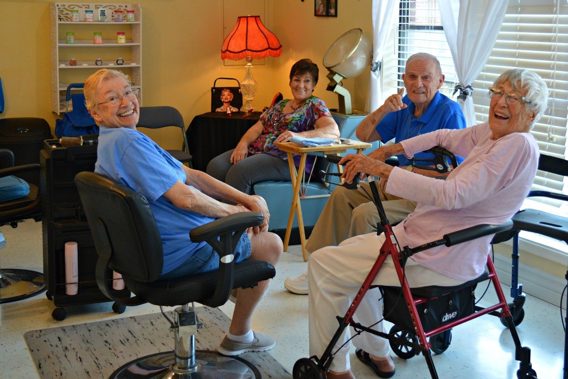 Four older adults laughing together in a salon-like setting. One uses a walker.