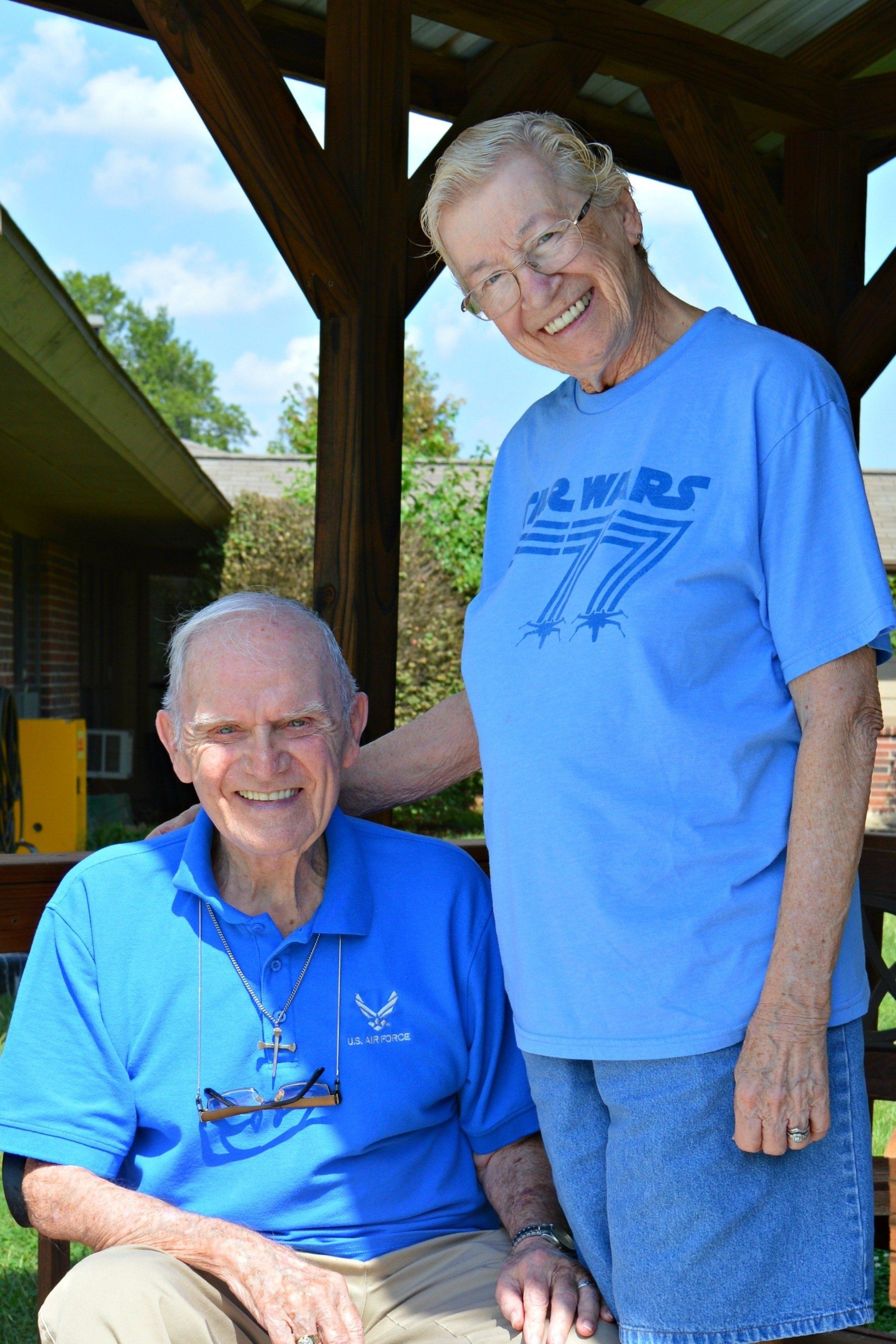 Elderly couple smiling together outdoors. The woman is wearing a Star Wars shirt.