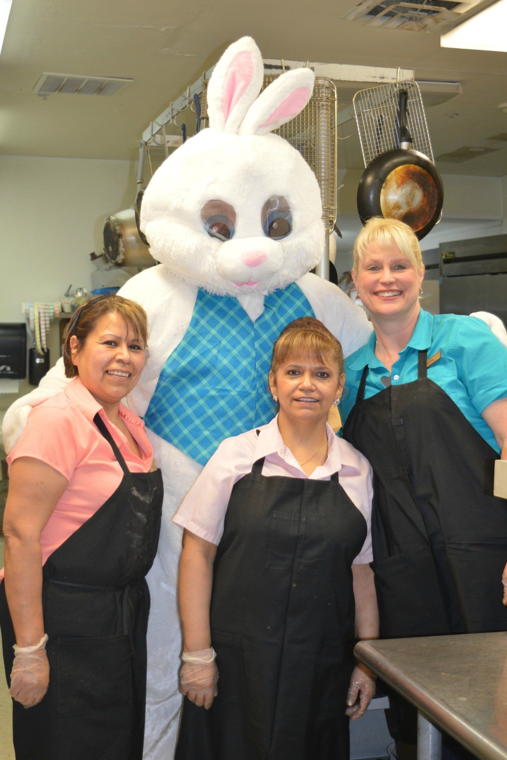 Easter Bunny poses with three women in a commercial kitchen; everyone is smiling.