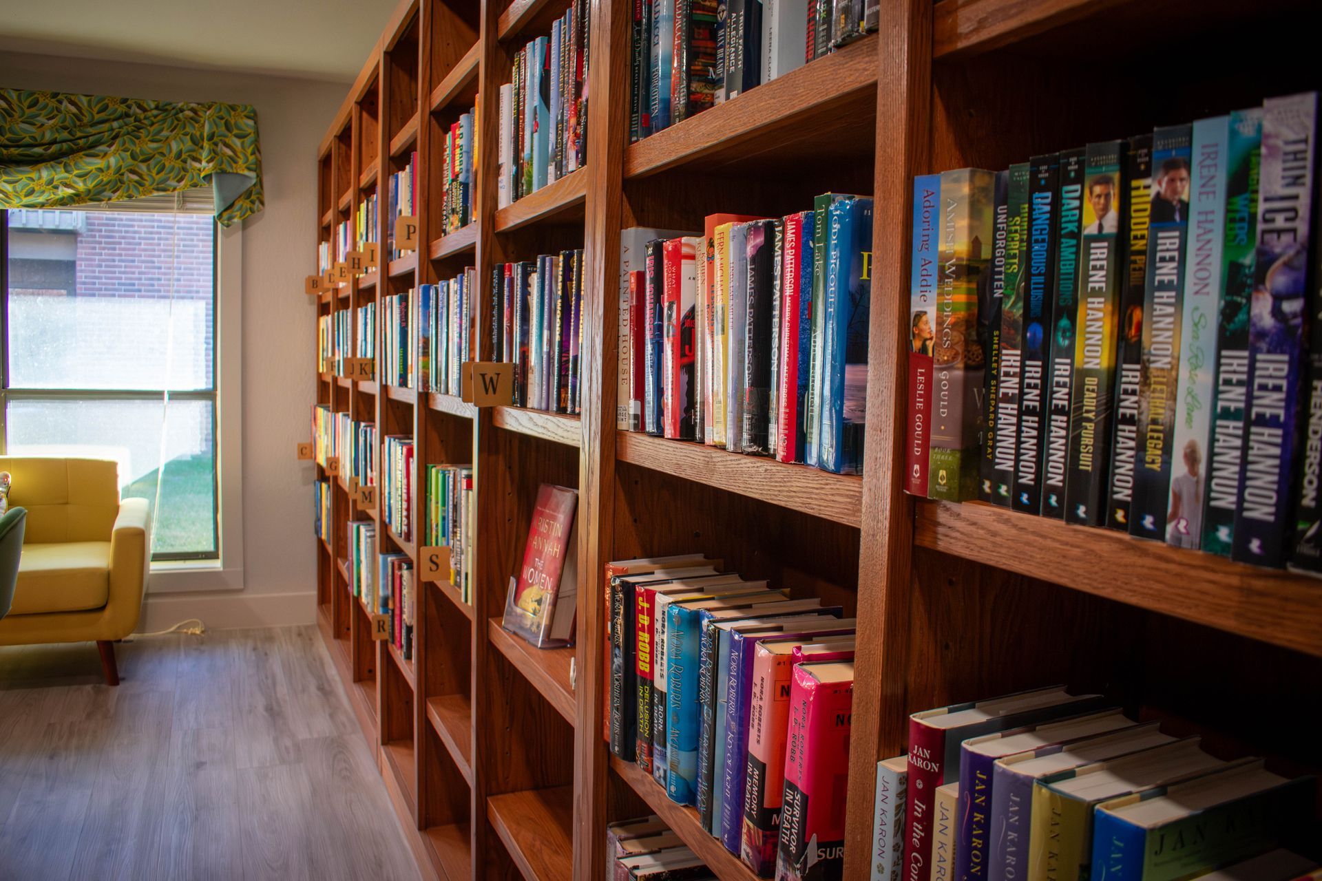 Wooden bookshelves filled with books in a room; a yellow chair sits near a window.
