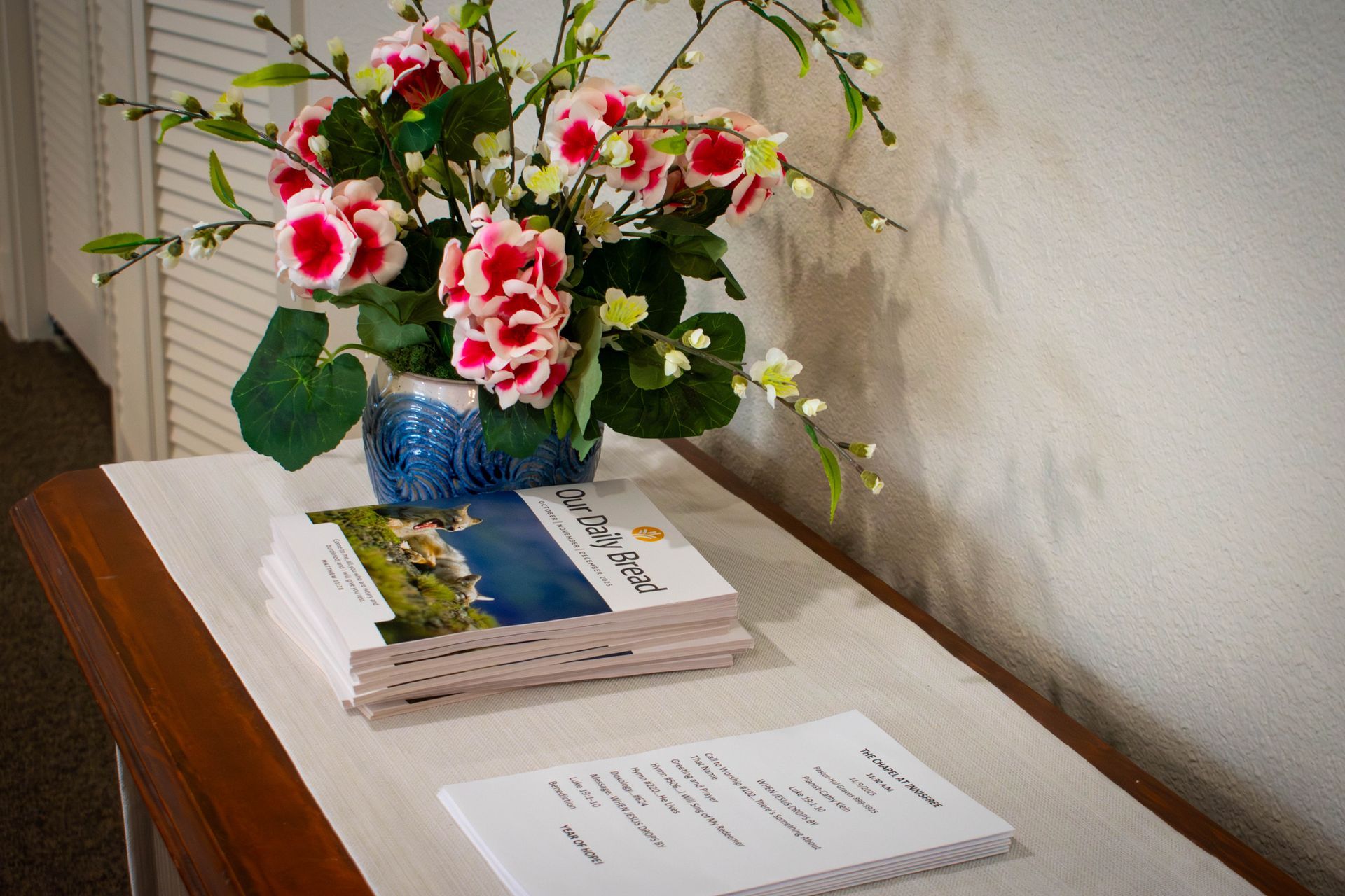 A bouquet of pink flowers sits on a table, with a stack of magazines and papers.