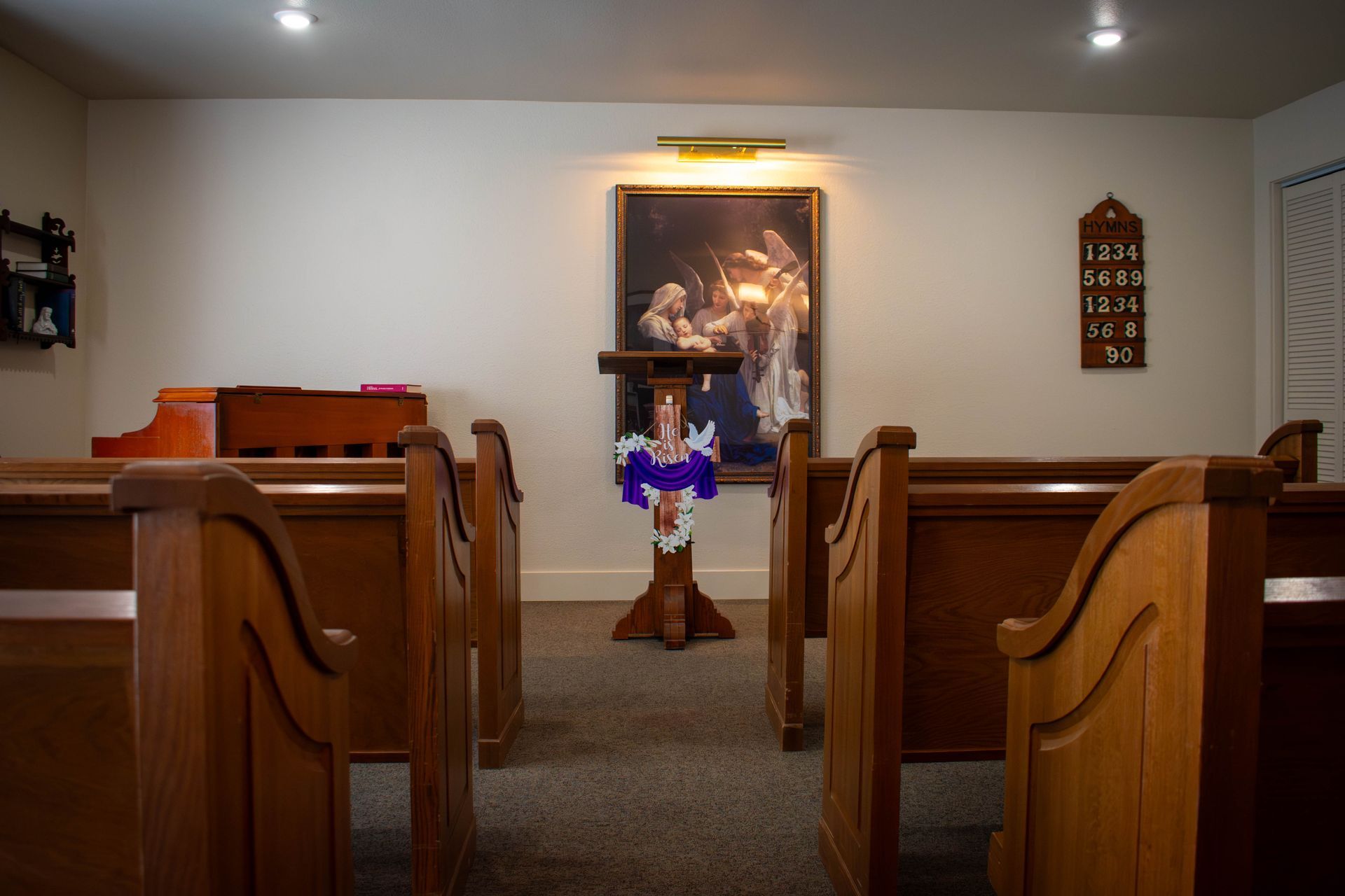 A church interior with wooden pews facing a central podium with a painting on the wall behind it.