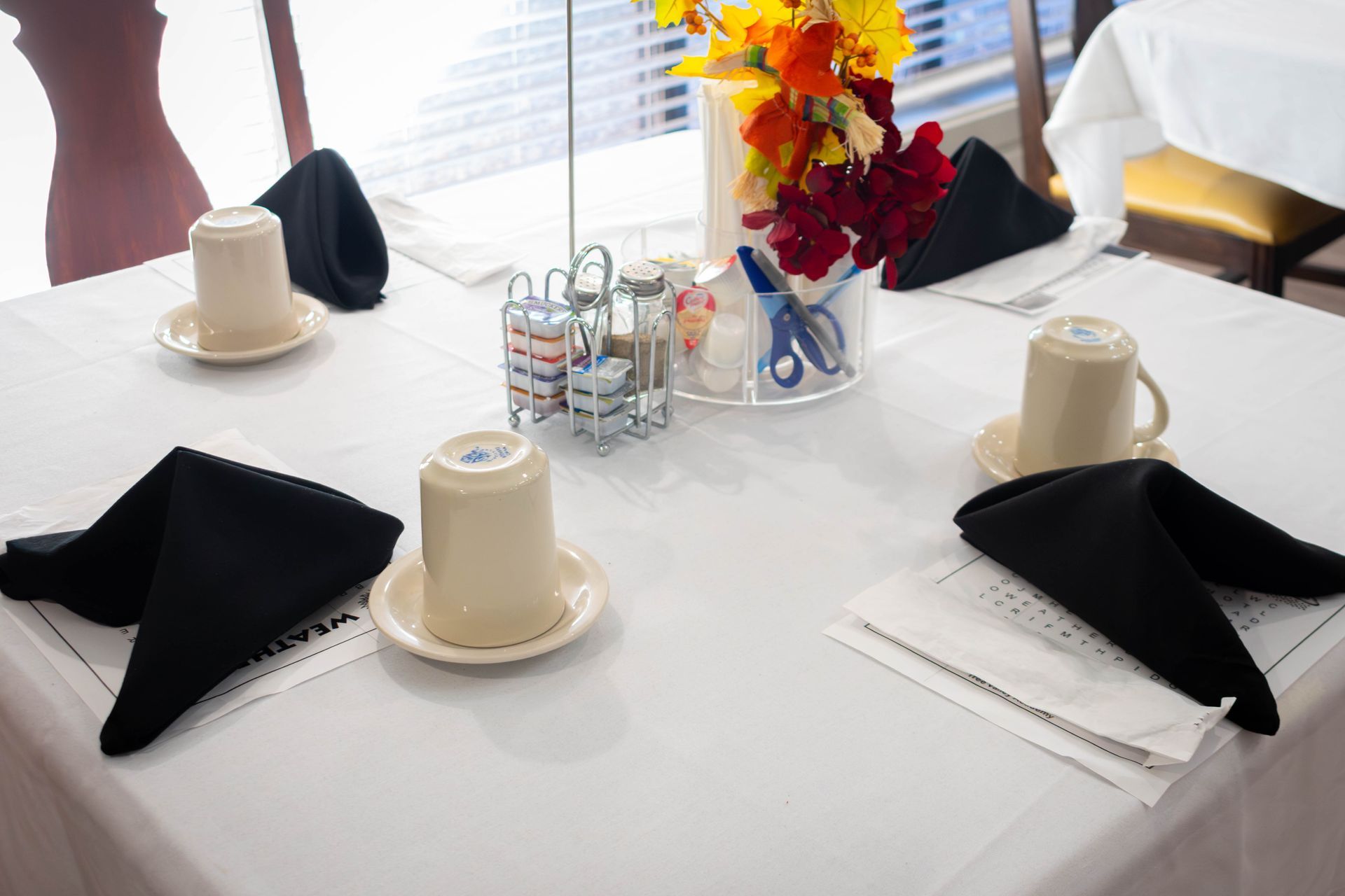 Table set for four with white tablecloth, black napkins, and flowers.