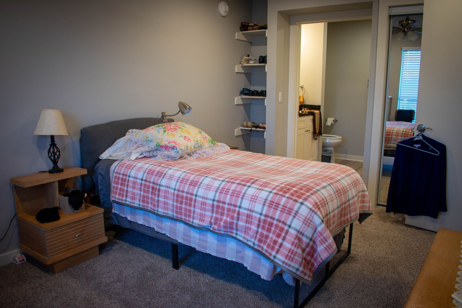 Bedroom with bed, nightstand, and doorway to bathroom. Gray walls, plaid comforter.