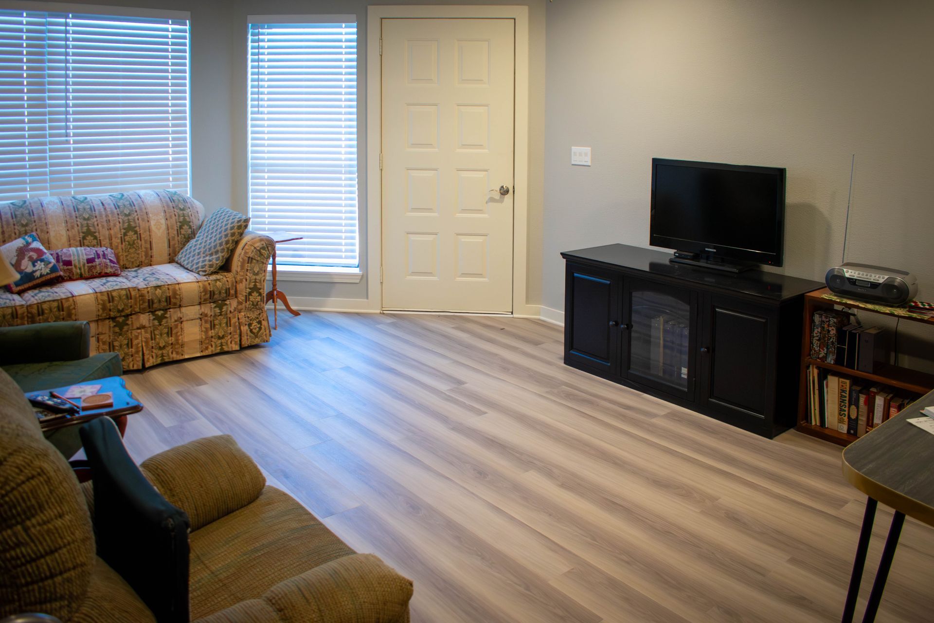 Living room with light wood floors, two couches, TV, and door.