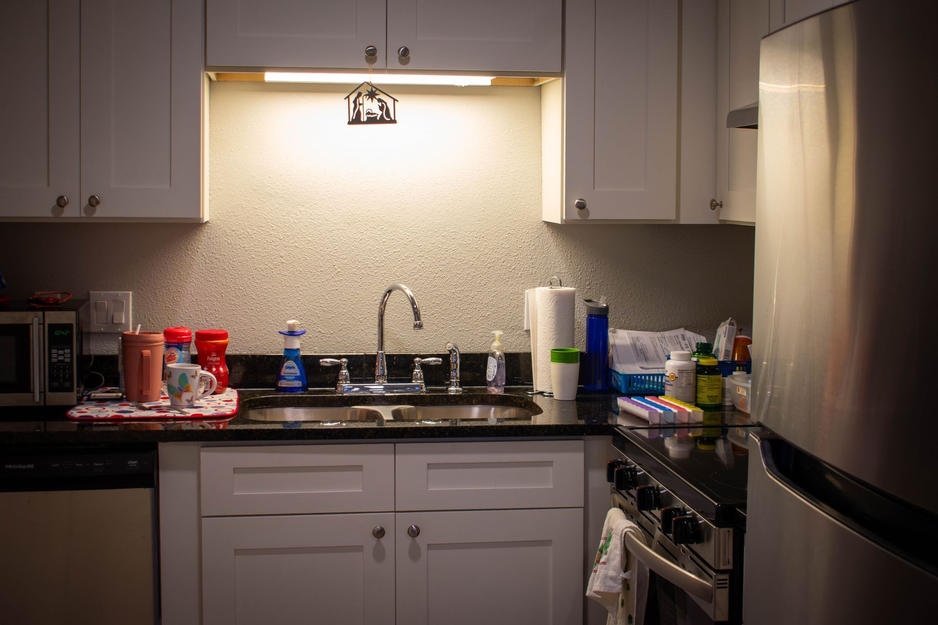 Kitchen with white cabinets, black countertop, stainless steel sink and refrigerator.