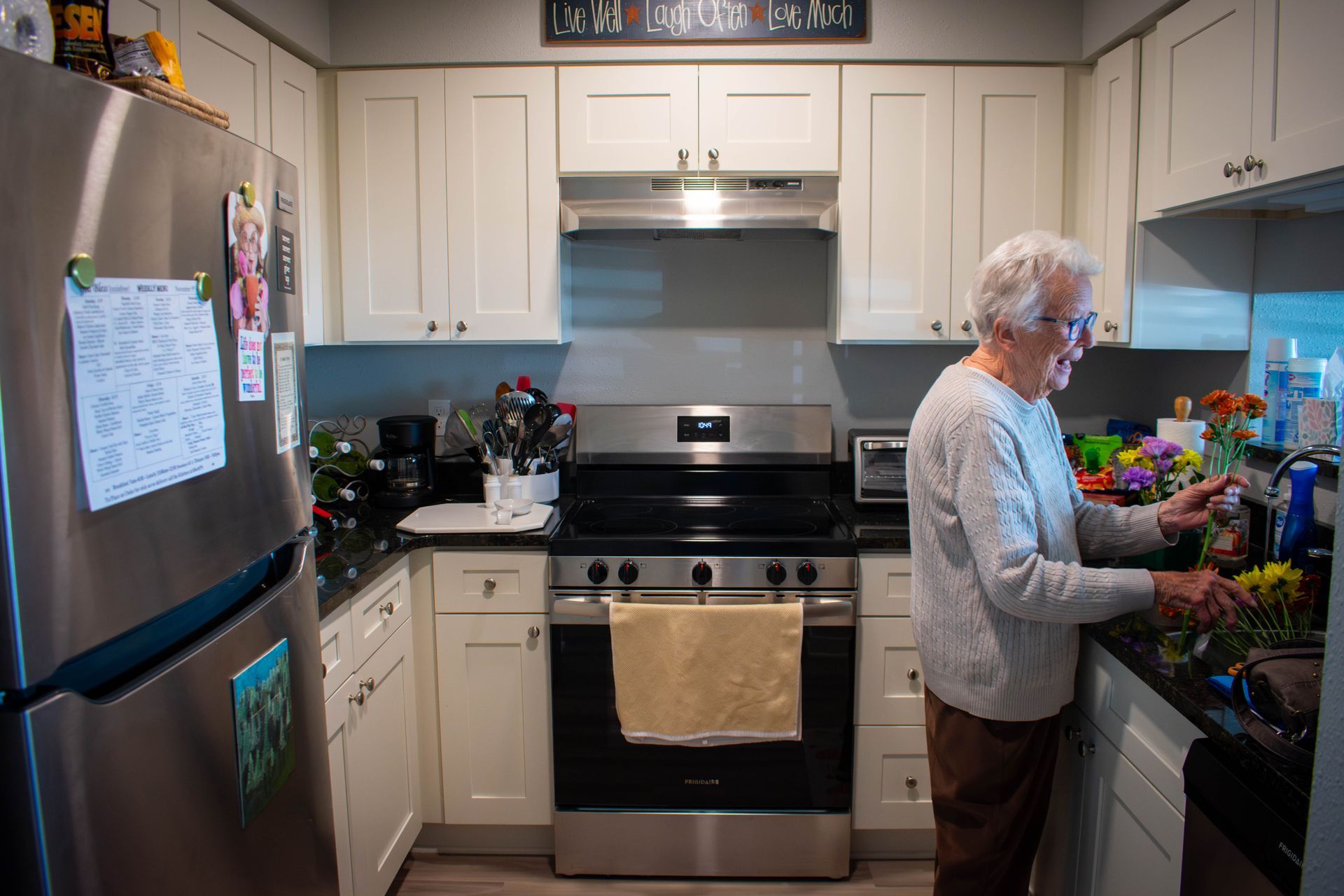 Woman in a kitchen, arranging flowers. Stainless steel appliances, white cabinets, and a black countertop.