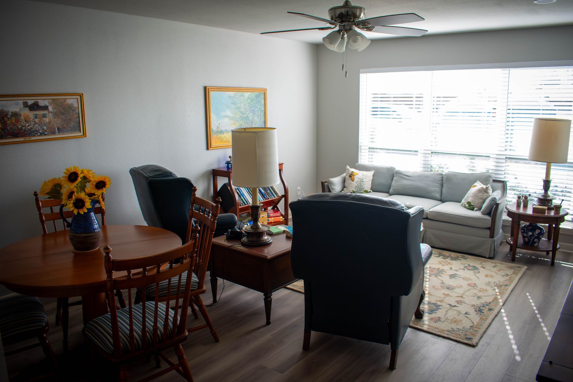 Living room with wood floors, blue sofa, round dining table, and various antique furniture.