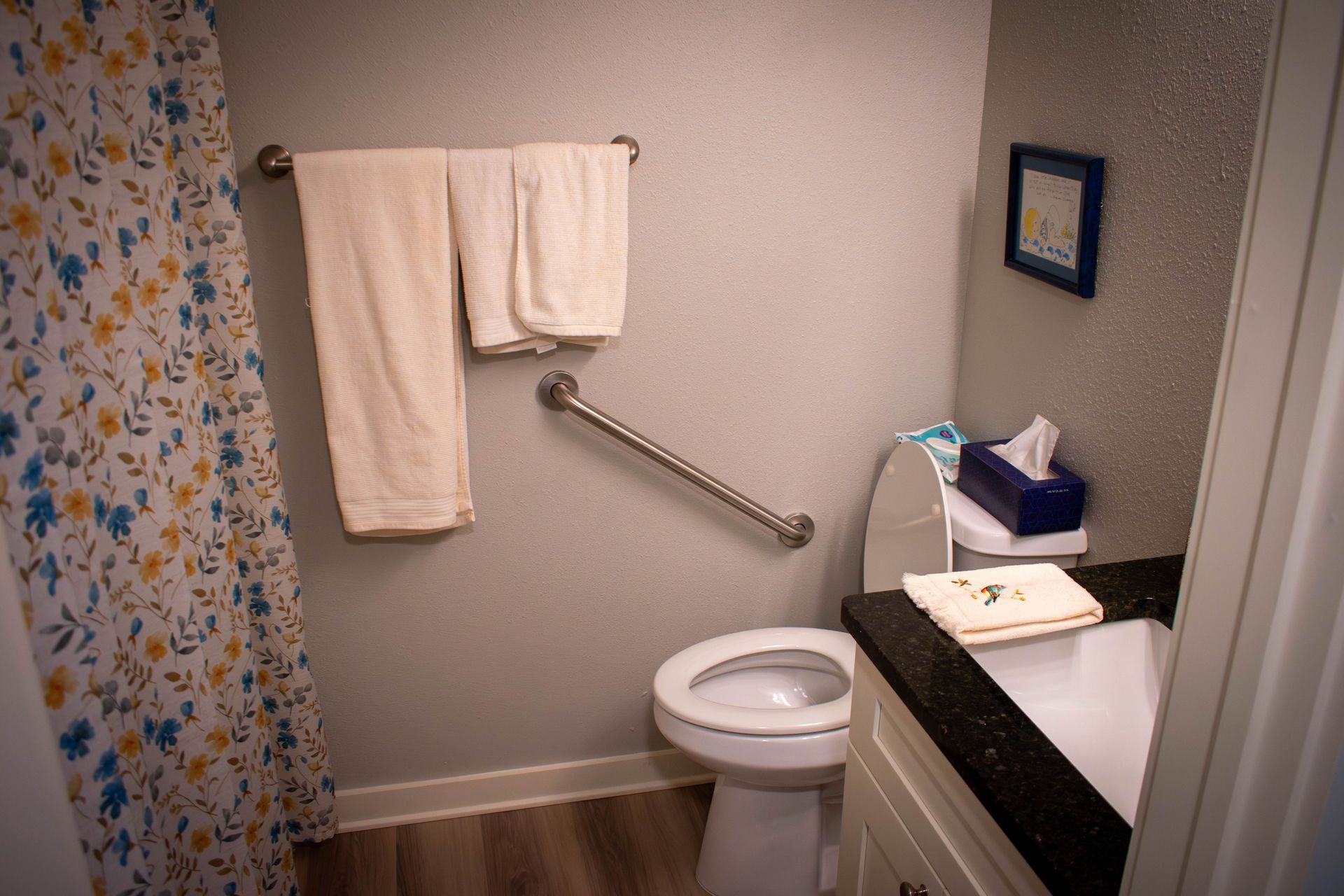 Small bathroom with toilet, sink, shower curtain, towels, and a grab bar.