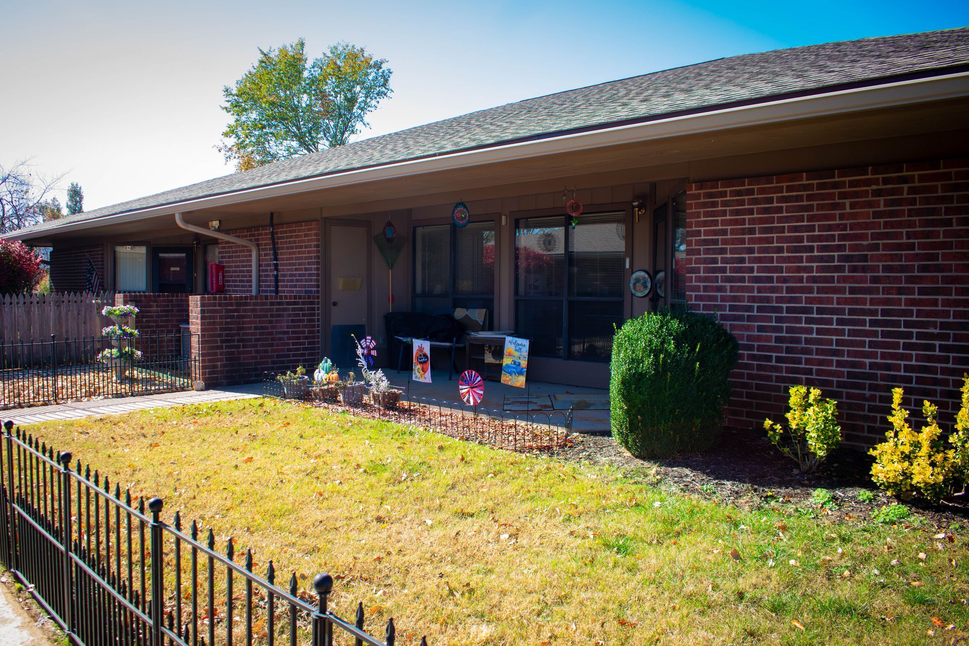 Brick building with porch, lawn, and small bushes. Decorative items on porch.
