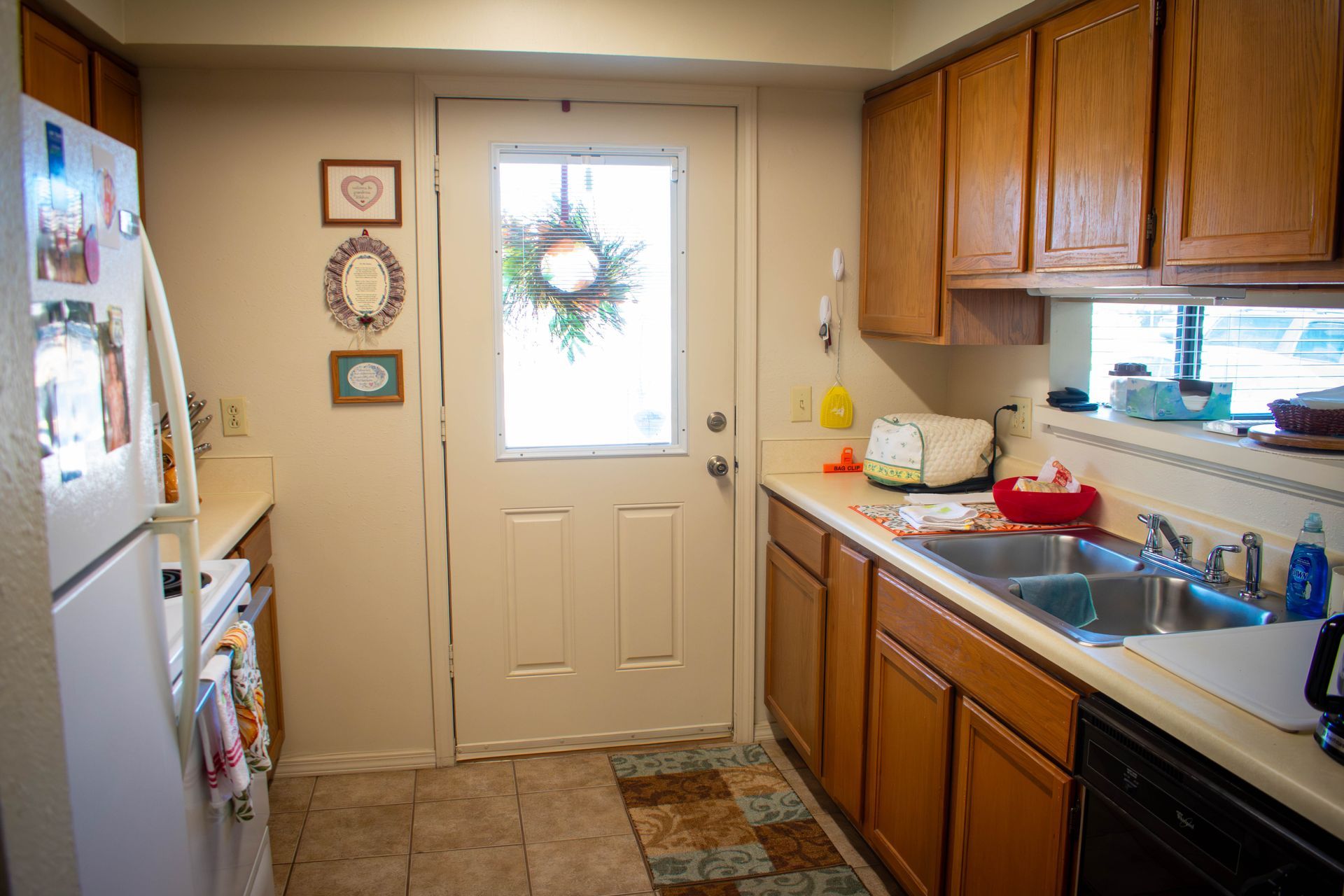 Kitchen with wooden cabinets, a white refrigerator, and a door with a wreath.