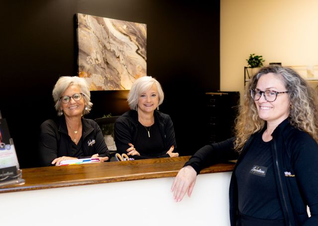 Three women are standing at a reception desk in a dental office.