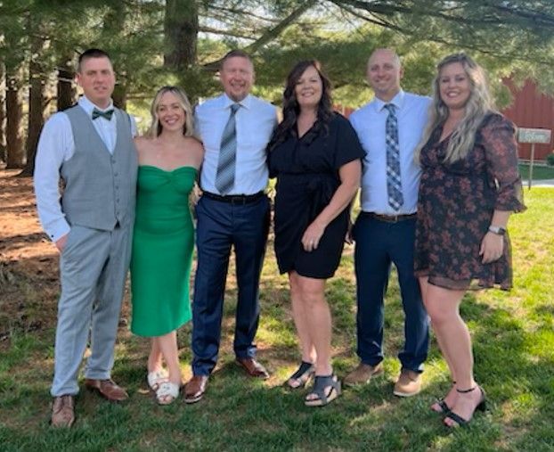 Woman in straw hat smiles, holding wine glass near a lake.