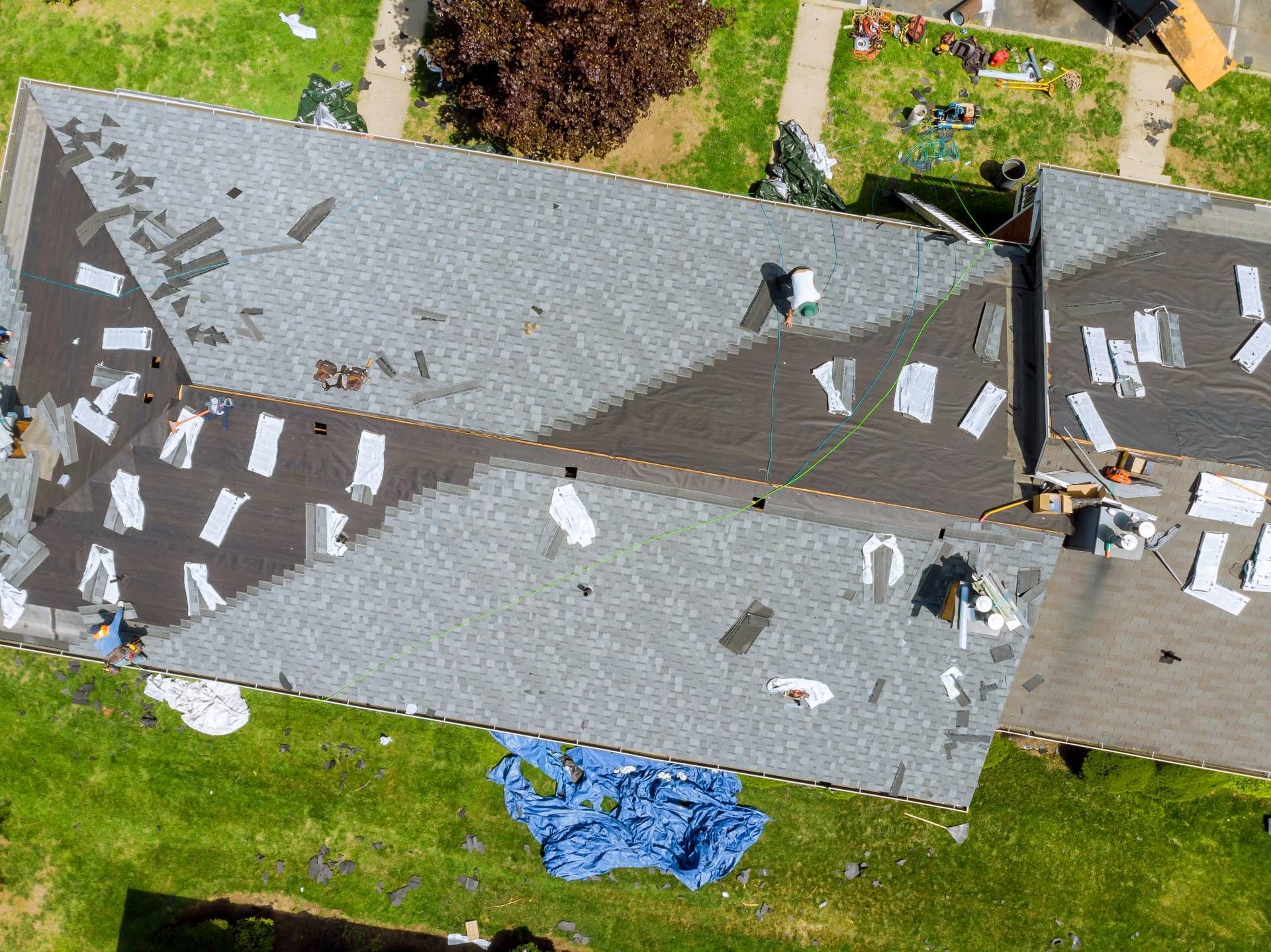 An aerial view of a residential roof undergoing repair, with gray shingles partially installed over black roofing felt.