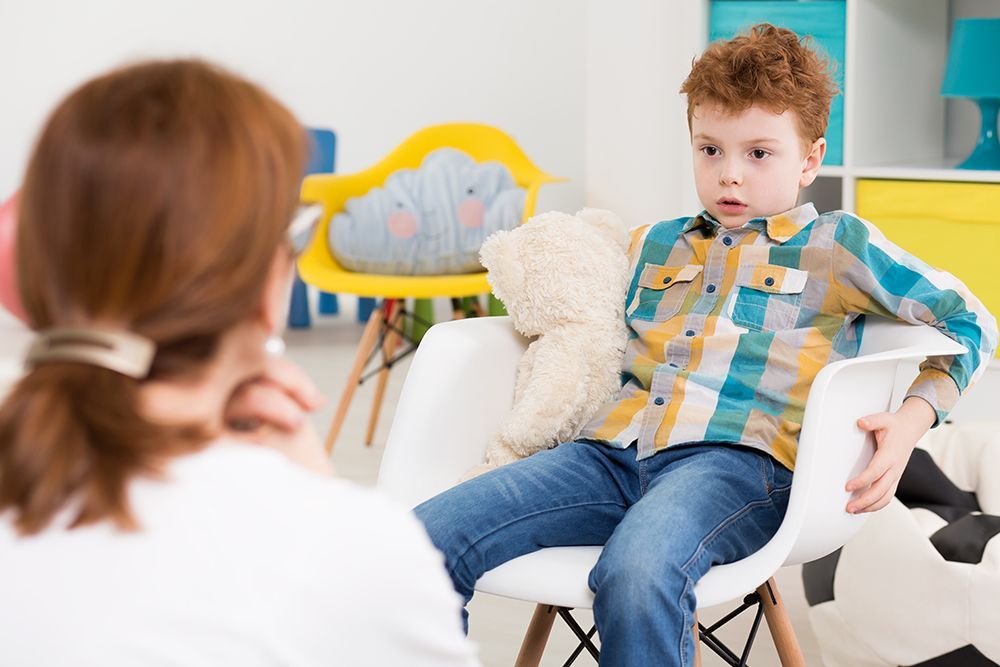 Person sitting in a white chair during a therapy session, facing a counselor in a bright room