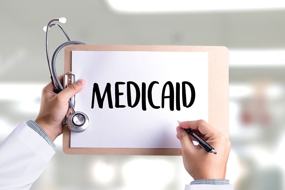 Clipboard with “MEDICAID” held by hands with a stethoscope, suggesting healthcare coverage.