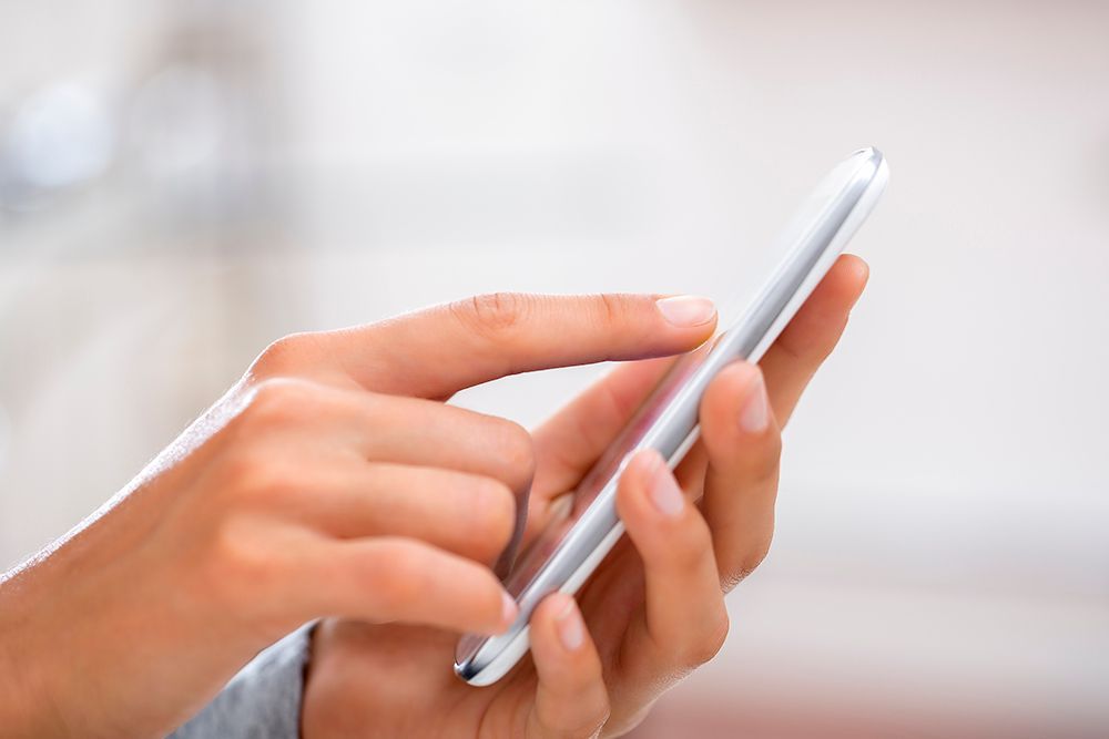 A close-up of a person's hands using a slim, white smartphone, with one finger touching the screen.