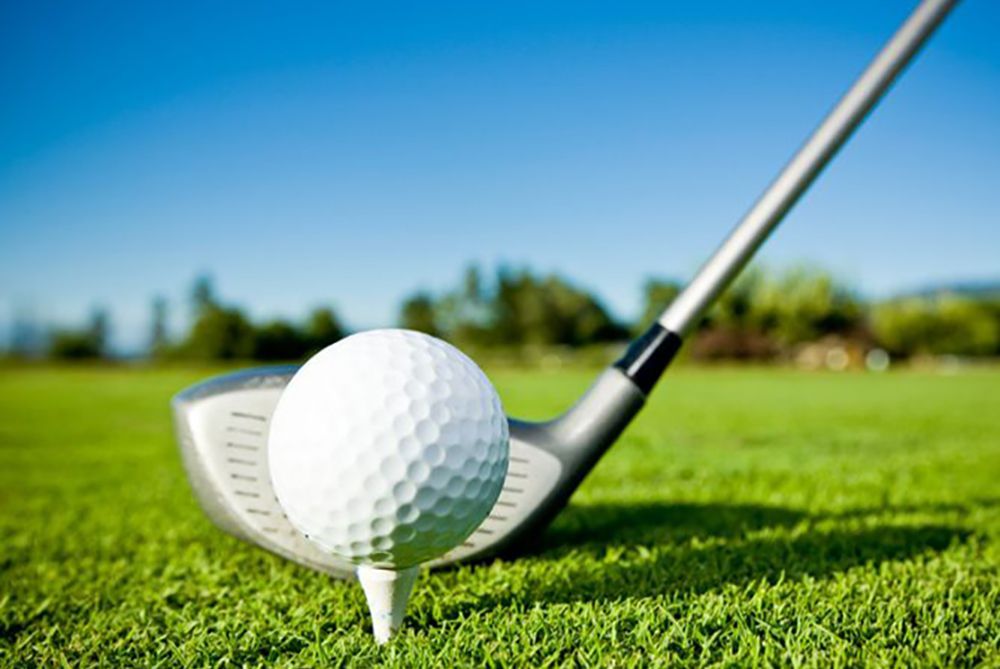Golf ball on a tee with a club behind it on a sunny green fairway