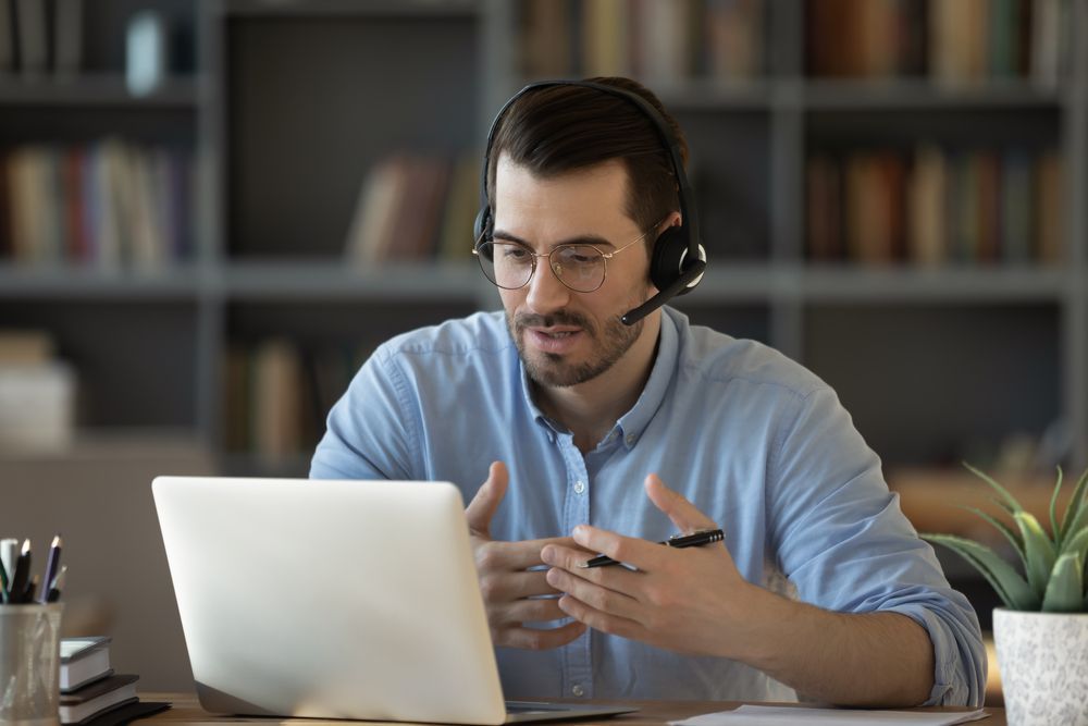 Man at desk with headset talking and participating in virtual meeting