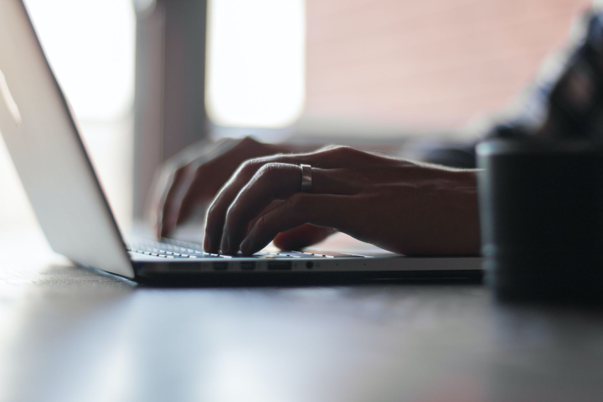 Person typing on laptop in dimly lit room, only shows hands on keyboard