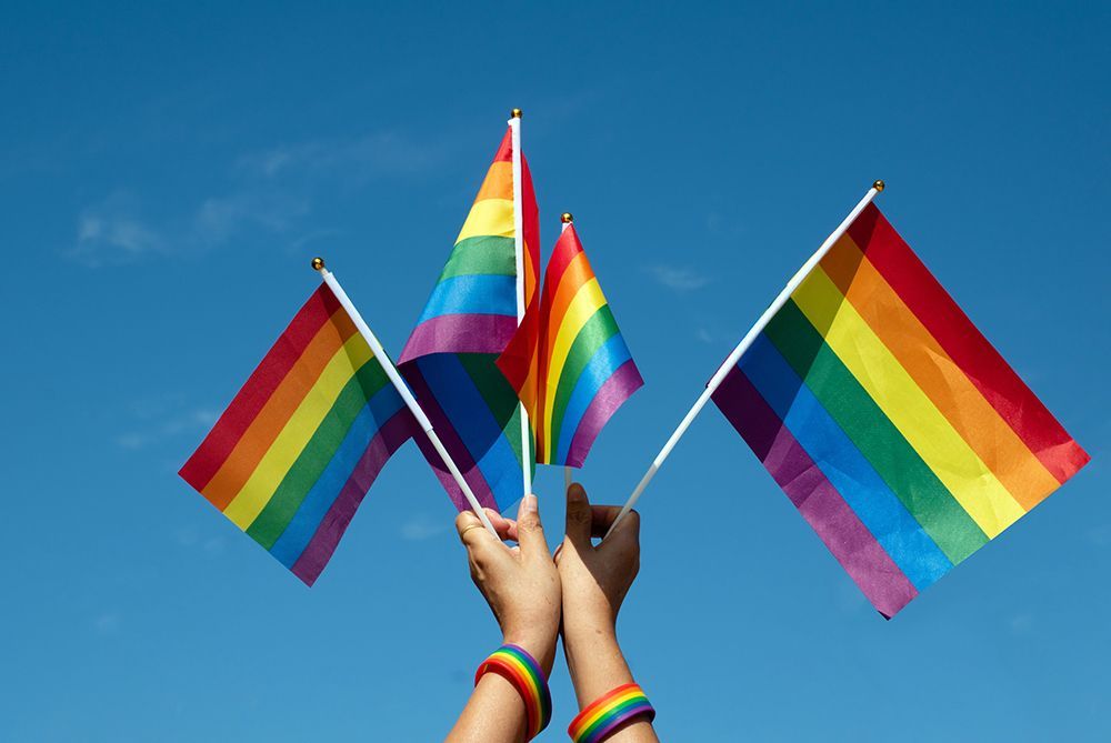 Hands holding rainbow Pride flags against a clear blue sky