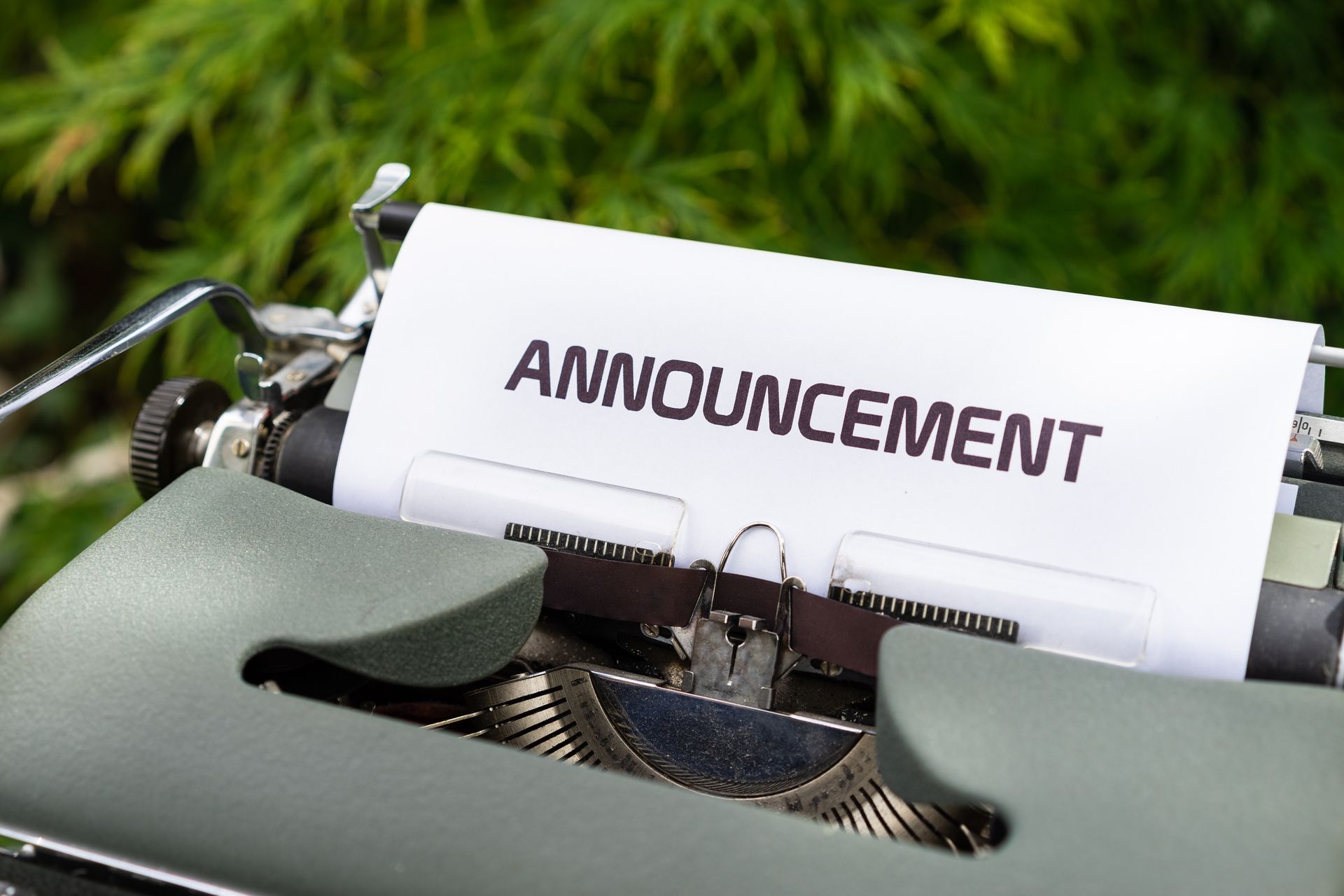 Typewriter with paper labeled “ANNOUNCEMENT” on a green outdoor background