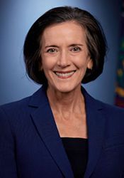 Studio headshot of a smiling woman in a blue blazer against a dark blue background