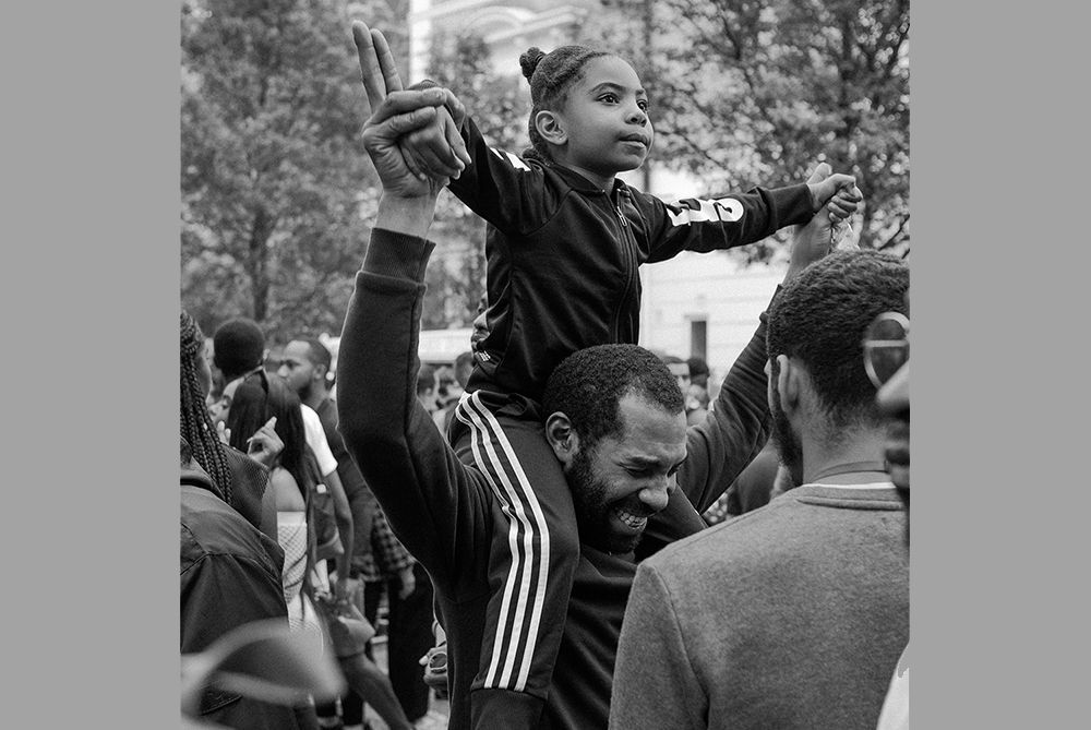 A Black man holding up a young girl on his shoulders in celebration