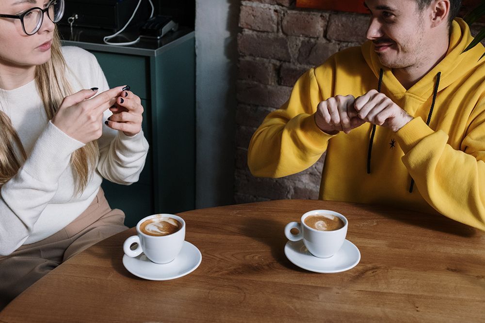 Man and woman using sign language to communicate while drinking coffee