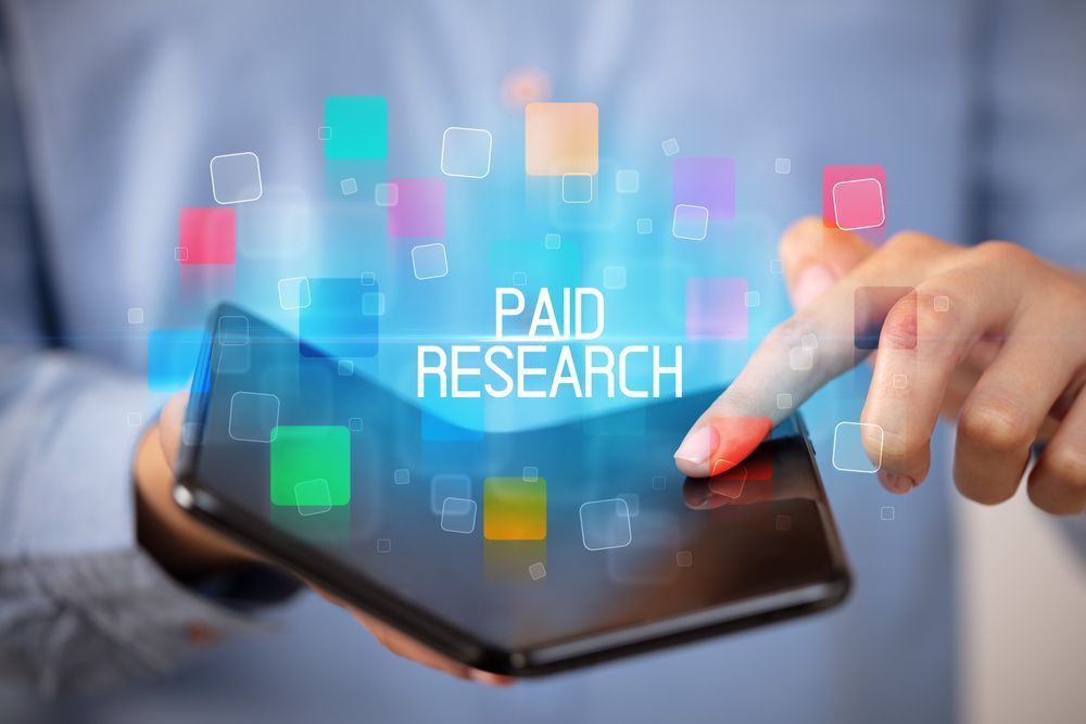 Hand tapping tablet with “PAID RESEARCH” text and colorful digital icons overlayed