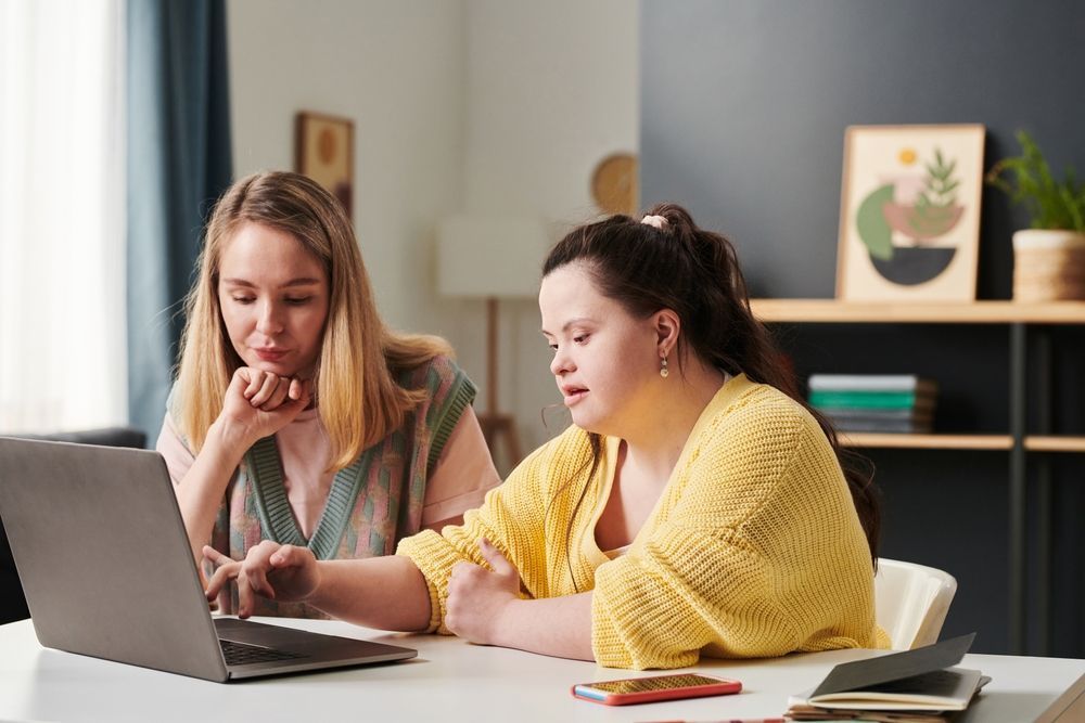Instructor working with employee with IDD on laptop