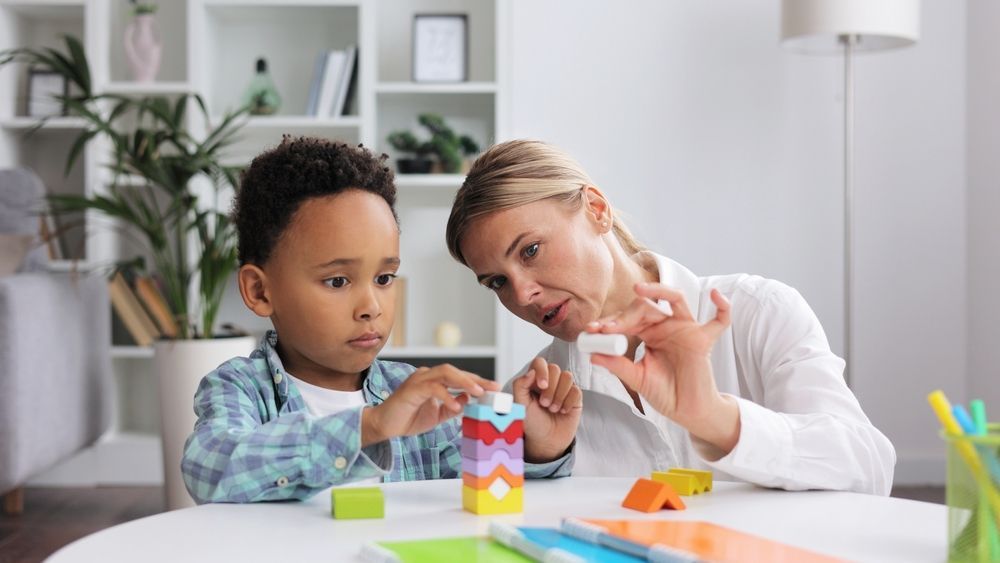 Adult and child building a colorful block tower at a table in a bright room