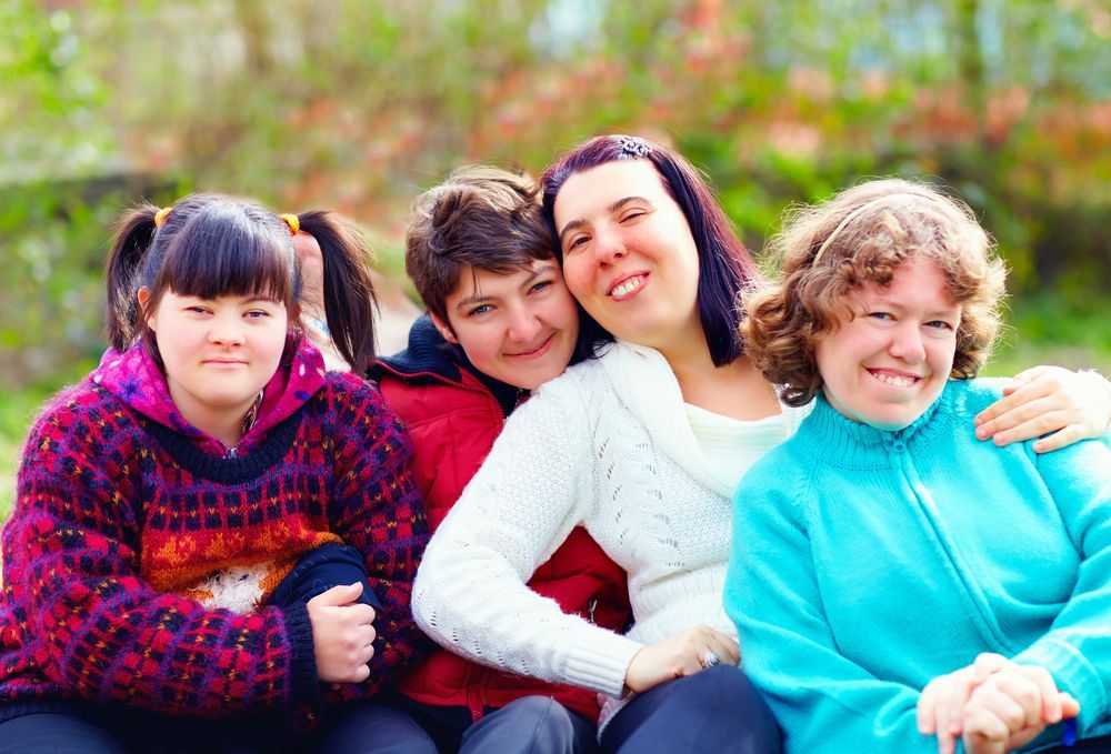 Four women with IDD smiling and standing side by side outdoors