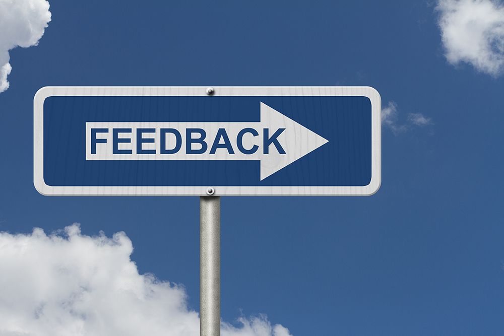Blue sign reading “FEEDBACK” with a white right-pointing arrow against a cloudy sky